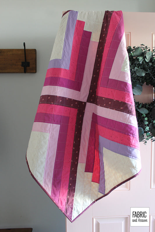 Sugar pop quilt hanging from a pink door with a green wreath. The quilt is bright pink, magenta, light pink, lavender, and beige.